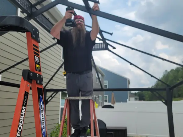 Technician on a ladder bolting together the frame of an outdoor pergola