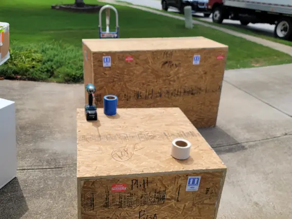 Two finished crates marked and stacked on a driveway with the moving truck waiting at the curb