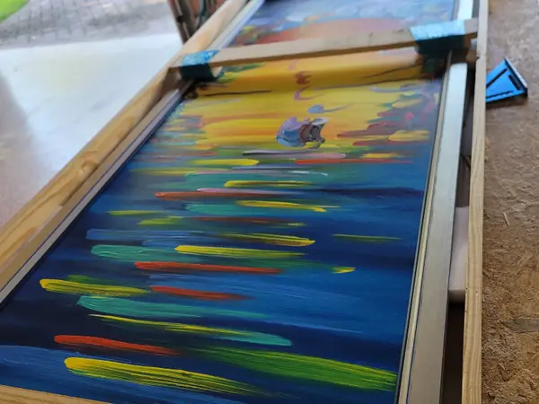 Large framed painting sitting in an open custom wood travel frame on a driveway