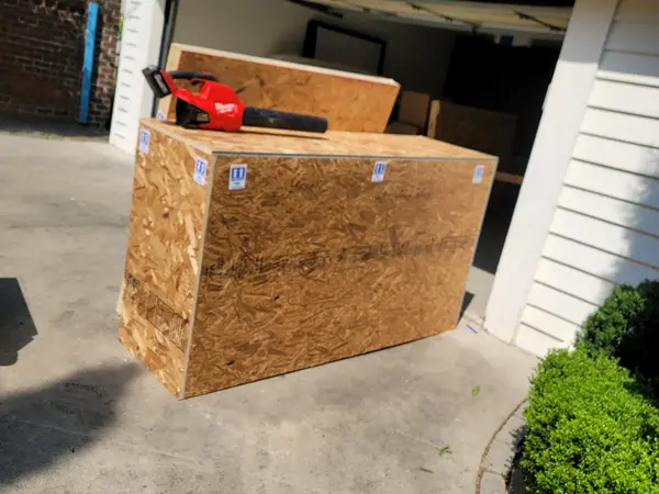 Finished sheathed crate standing outside an open garage with the saw still resting on the lid
