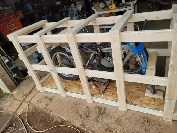 Custom wooden crate frames stacked in a garage beside a motorcycle awaiting crating