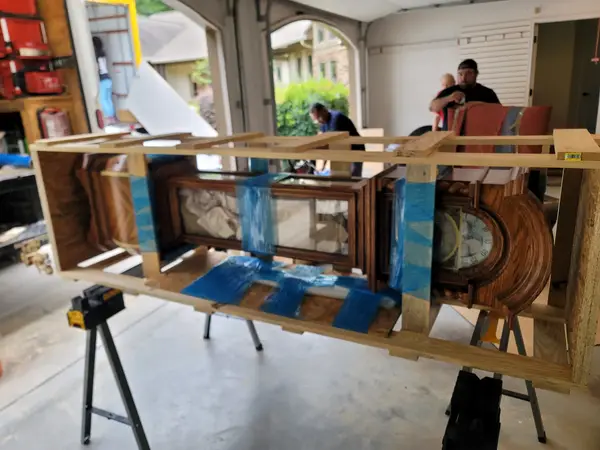 Antique grandfather clock laid on sawhorses inside a custom lumber crate frame with its glass panels taped