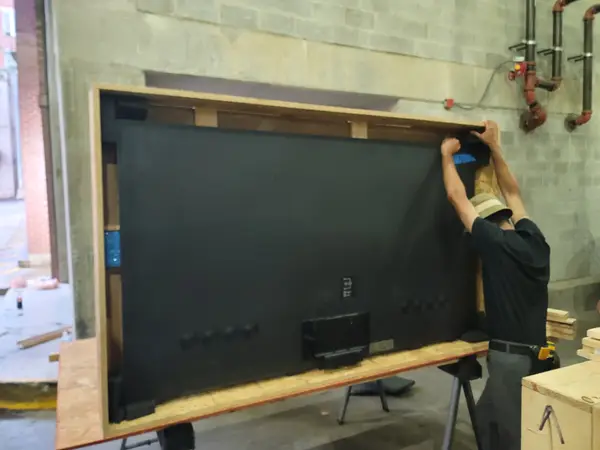 Large flat-screen TV framed in timber for transport, taped and braced on sawhorses