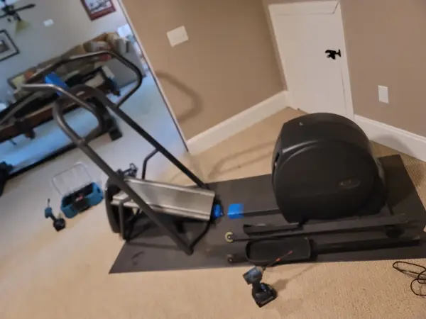 Elliptical and treadmill part-assembled on a protective mat in a spare room