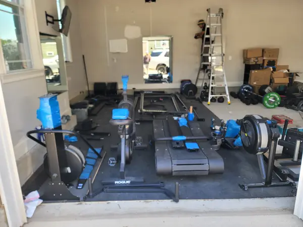 Full home gym laid out mid-assembly with a rack, treadmill, rower and bike across the floor