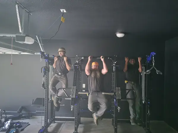 Three technicians hanging from a newly assembled power rack in a garage gym to check it under load