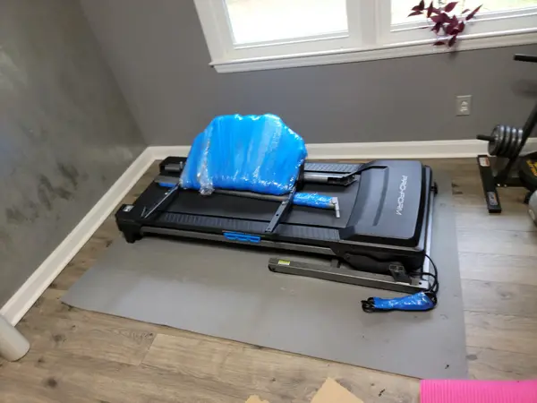 New treadmill partially assembled and wrapped in protective plastic in a home gym