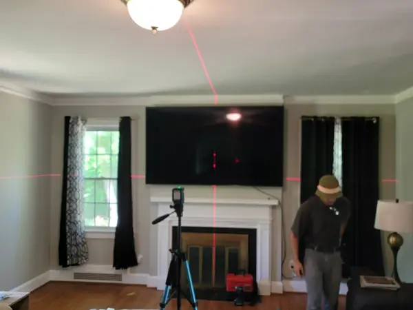 Technician setting a laser level on a tripod before mounting a TV above a fireplace