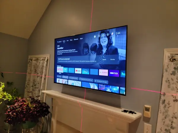 Flat-screen TV mounted level above a fireplace mantel with red laser level lines projected across the wall