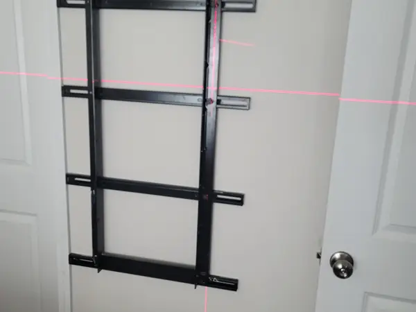TV wall bracket held on the wall with red laser level lines crossing it before the first hole is drilled