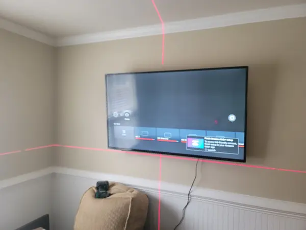 Flat-screen TV mounted in a room corner with red laser level lines confirming it is square
