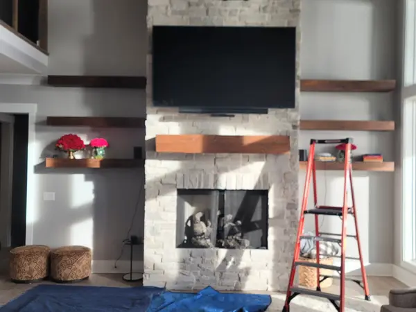 Large TV mounted high on a stacked stone fireplace in a two-story vaulted living room