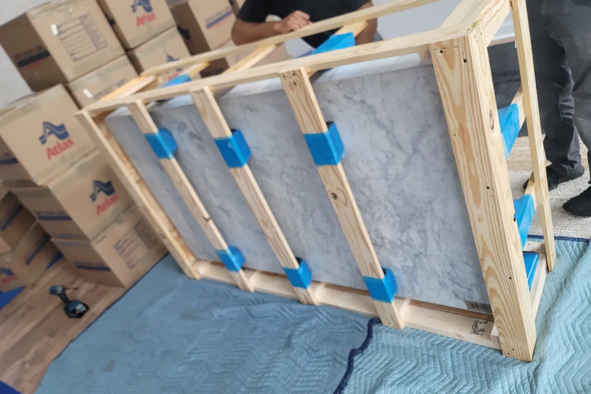 Marble tabletop braced inside a custom wood crate frame beside stacked moving cartons