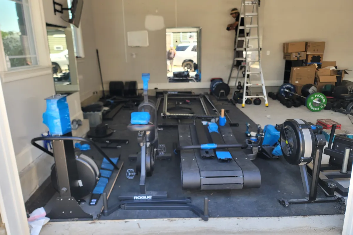 Full home gym laid out mid-assembly with a rack, treadmill, rower and bike across the floor