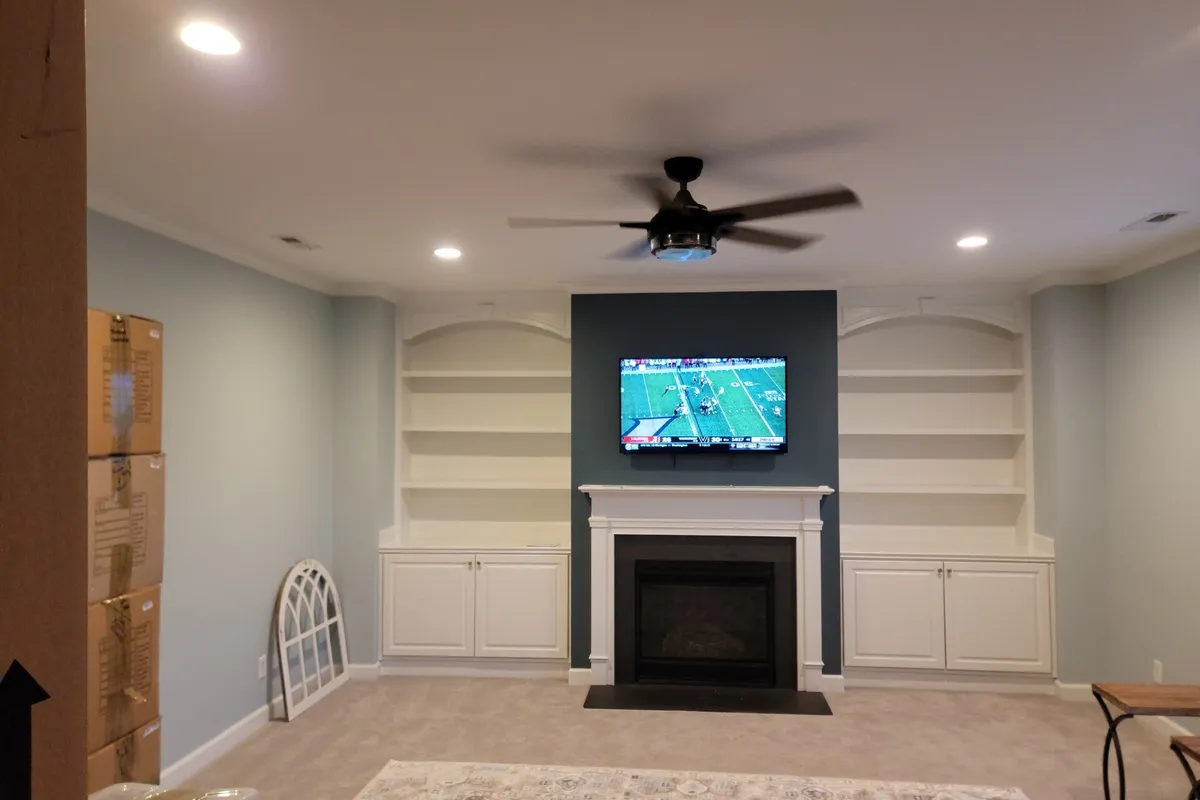 Large flat-screen TV mounted above a fireplace between white built-in cabinets